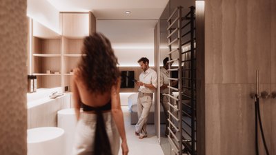 Photos from your hotel in Pfalzen in Val Pusteria/Pustertal Woman walking into modern bathroom, man reading phone in background