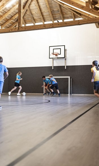 Kinder spielen Hallenfußball unter Dachbalken auf einem Spielfeld