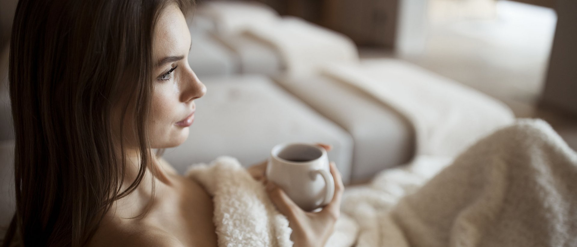 Woman relaxing on sofa with blanket holding a cup of tea