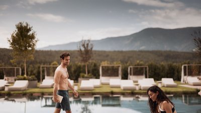 Mann und Frau am Pool mit Bergen im Hintergrund und Liegestühlen