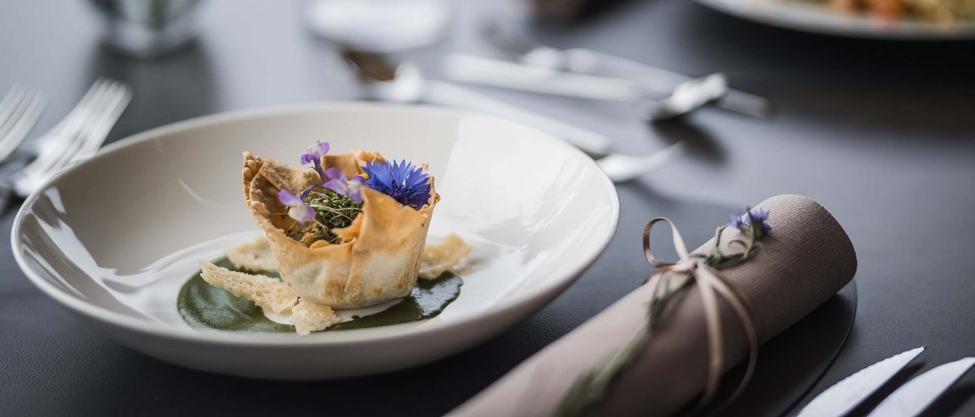Kunstvoll angerichtetes Gericht mit essbaren Blüten in weißem Teller auf gedecktem Tisch