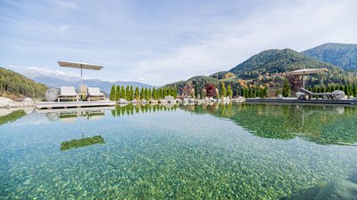 L’esclusività in foto: il nostro chalet in Alto Adige di lusso Piscina naturale con acqua limpida e lettini con ombrelloni in paesaggio montano