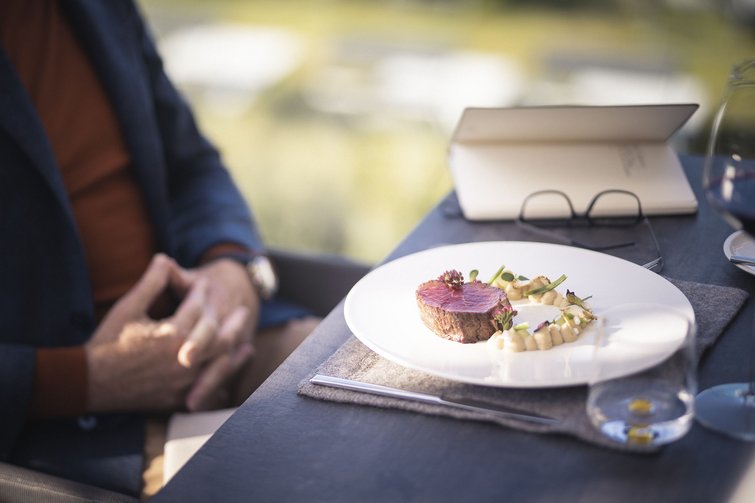 Gedeckter Tisch mit feinem Fleischgericht und Person im Hintergrund
