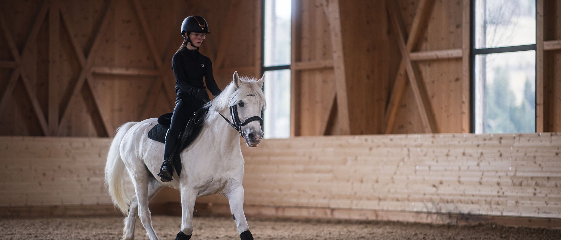 Il benessere nasce qui: il nostro hotel in Val Pusteria Cavaliere su cavallo bianco in maneggio con ostacoli colorati