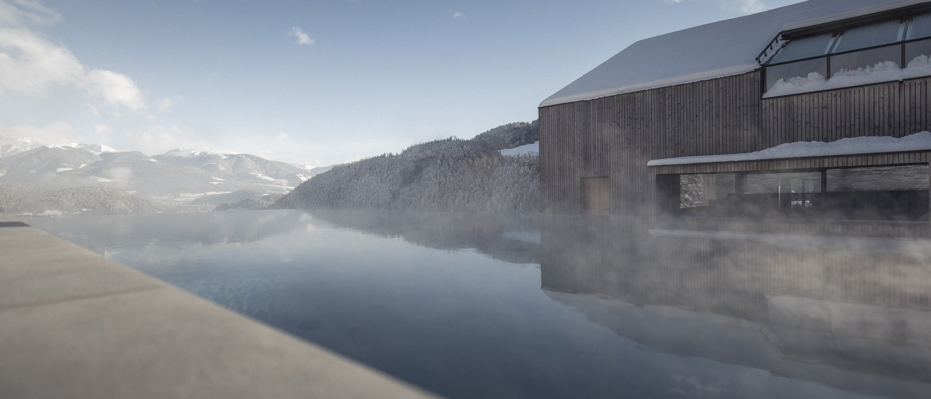 Wooden house with snow-covered roof beside a calm mountain lake