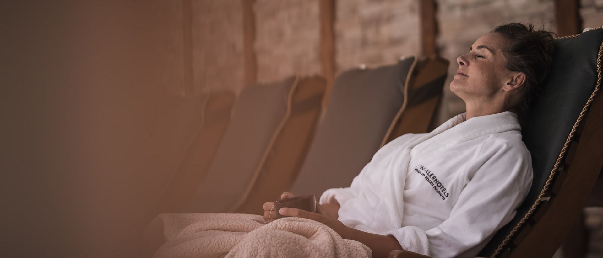 Frau entspannt in weißem Bademantel auf Liegestuhl mit Decke