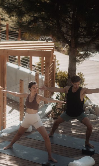 Zwei Personen praktizieren Yoga auf Holzterrasse neben Pool