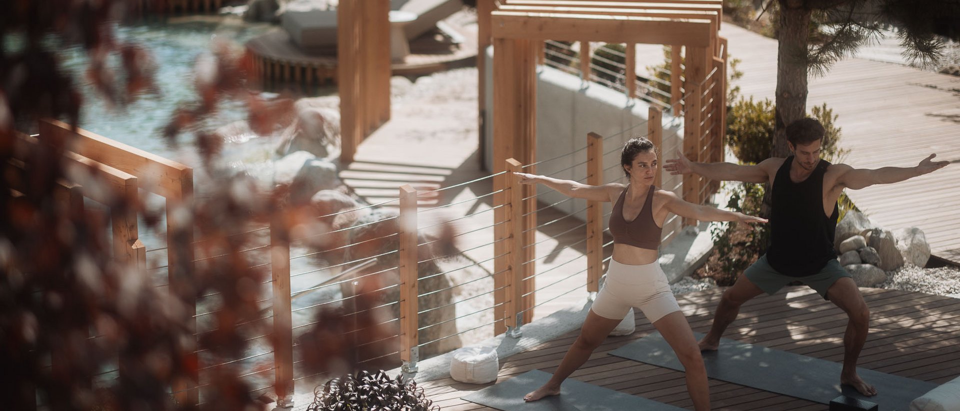 Zwei Personen praktizieren Yoga auf Holzterrasse neben Pool