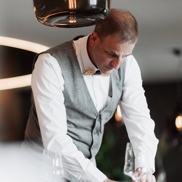 Una vacanza di relax nel nostro chalet di lusso in Alto Adige Uomo con gilet e papillon apparecchia un tavolo con bicchieri