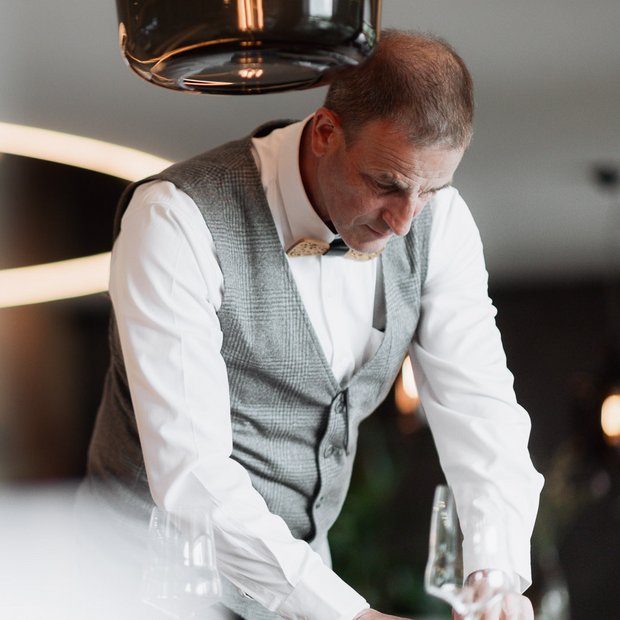 Mann in Weste und Fliege deckt Tisch mit Gläsern