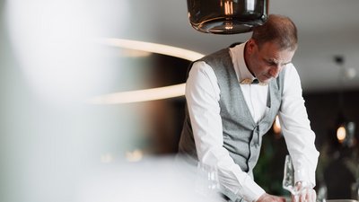 L’esclusività in foto: il nostro chalet in Alto Adige di lusso Uomo con gilet e papillon apparecchia un tavolo con bicchieri