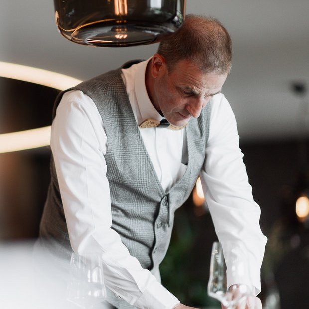 Man in vest and bow tie setting a table with glasses