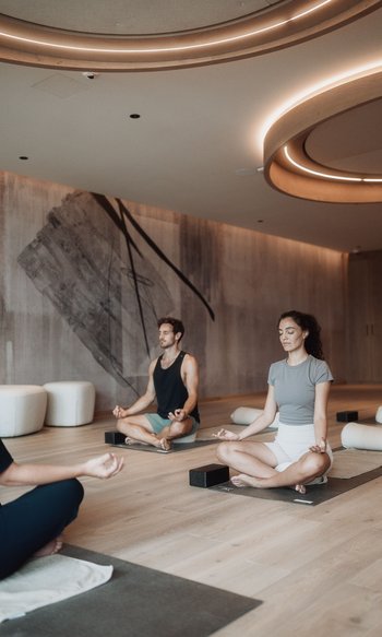 Menschen meditieren im Kreuzsitz auf Yogamatten in einem modernen Fitnessraum