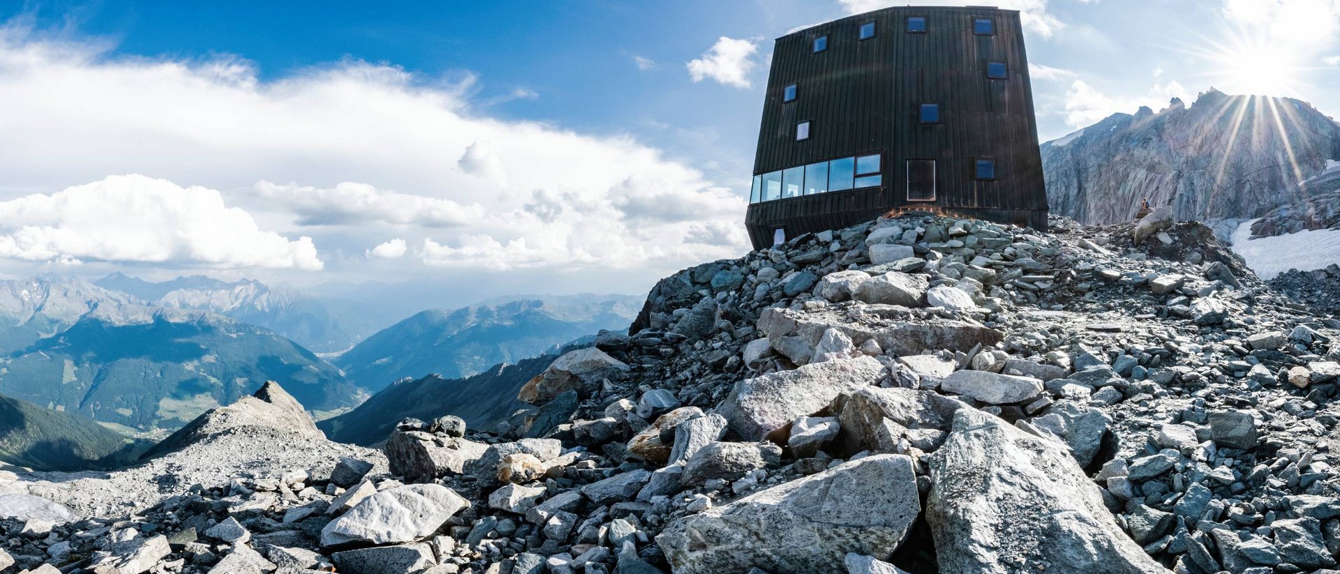 Casa di montagna moderna su cima rocciosa con cielo soleggiato e panorama