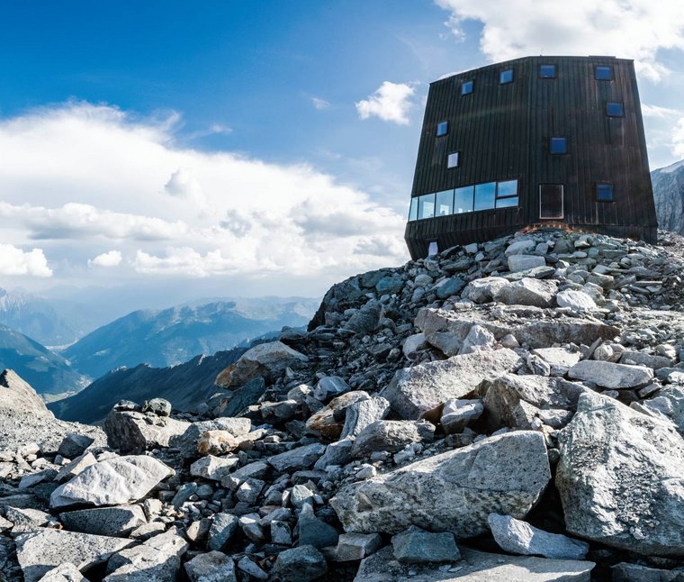 Casa di montagna moderna su cima rocciosa con cielo soleggiato e panorama