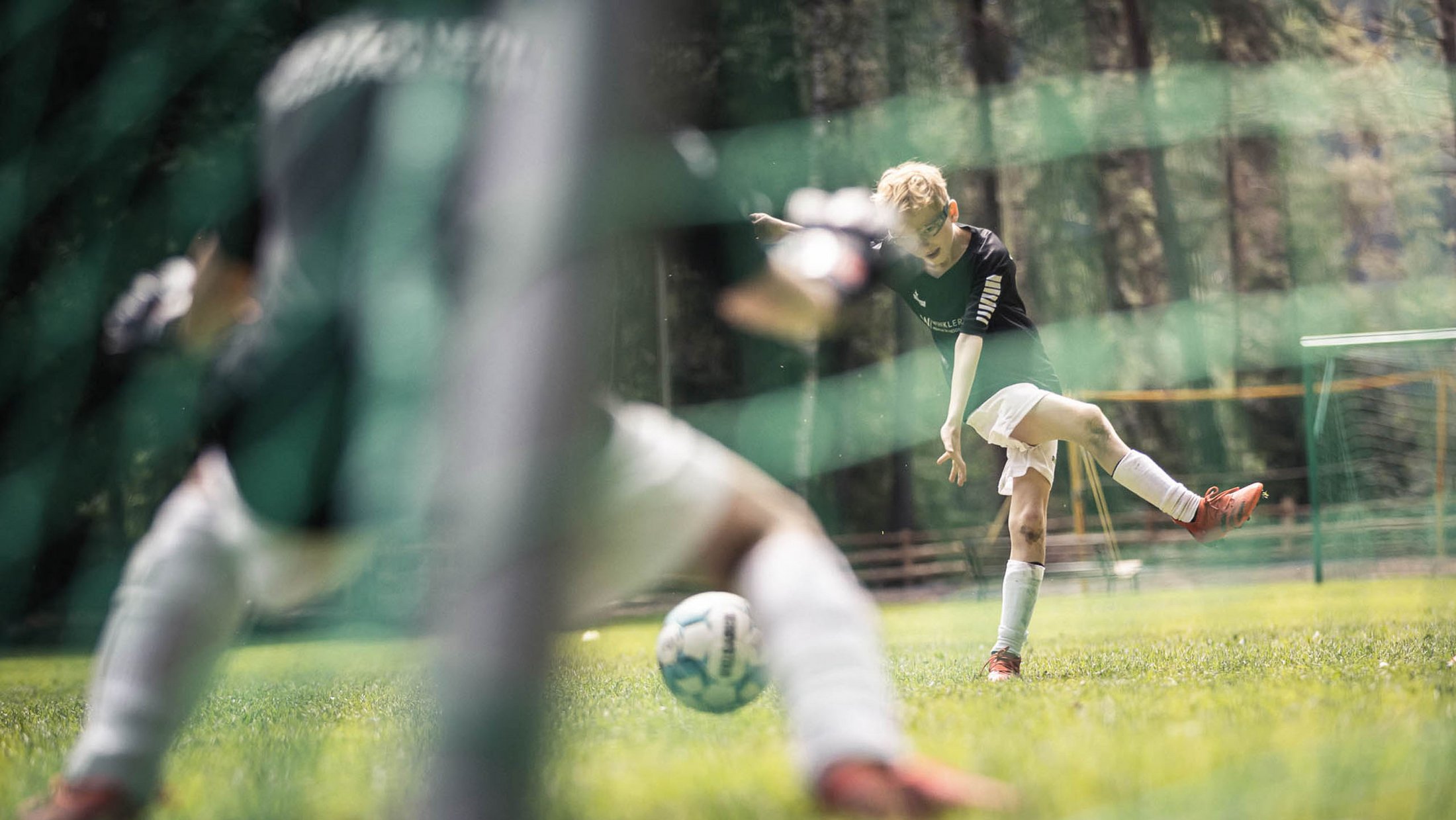 Giovane calciatore calcia il pallone verso la porta, portiere si prepara