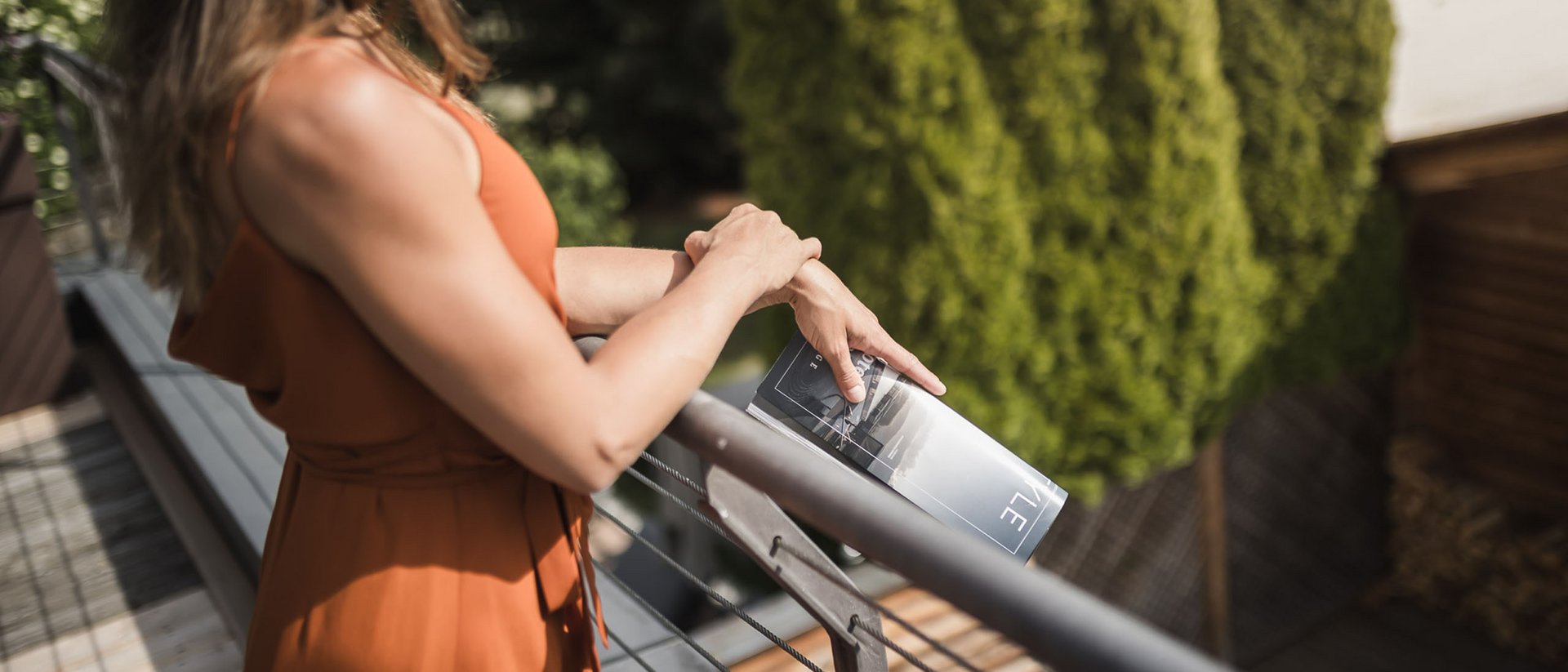 Frau im orangen Kleid lehnt an Balkon und hält Magazin in der Hand