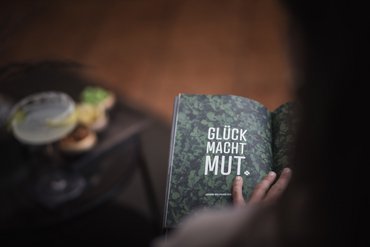 Mano che sfoglia pagina di libro con la citazione Felicità dà coraggio