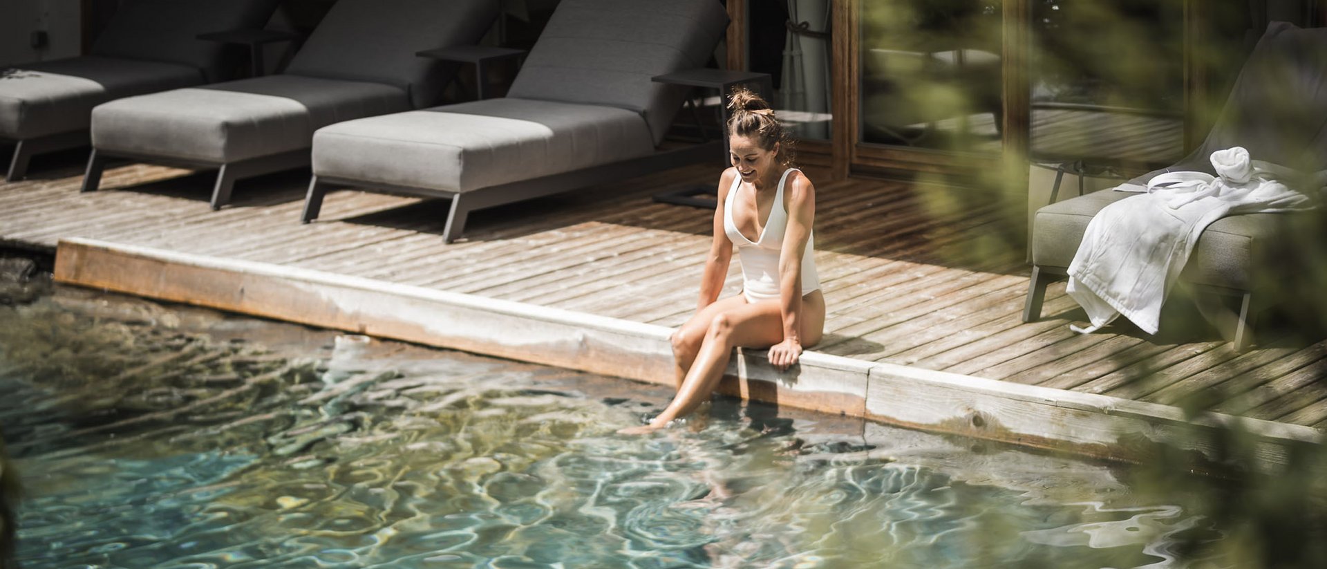 Donna in costume da bagno bianco seduta a bordo piscina con i piedi nell'acqua