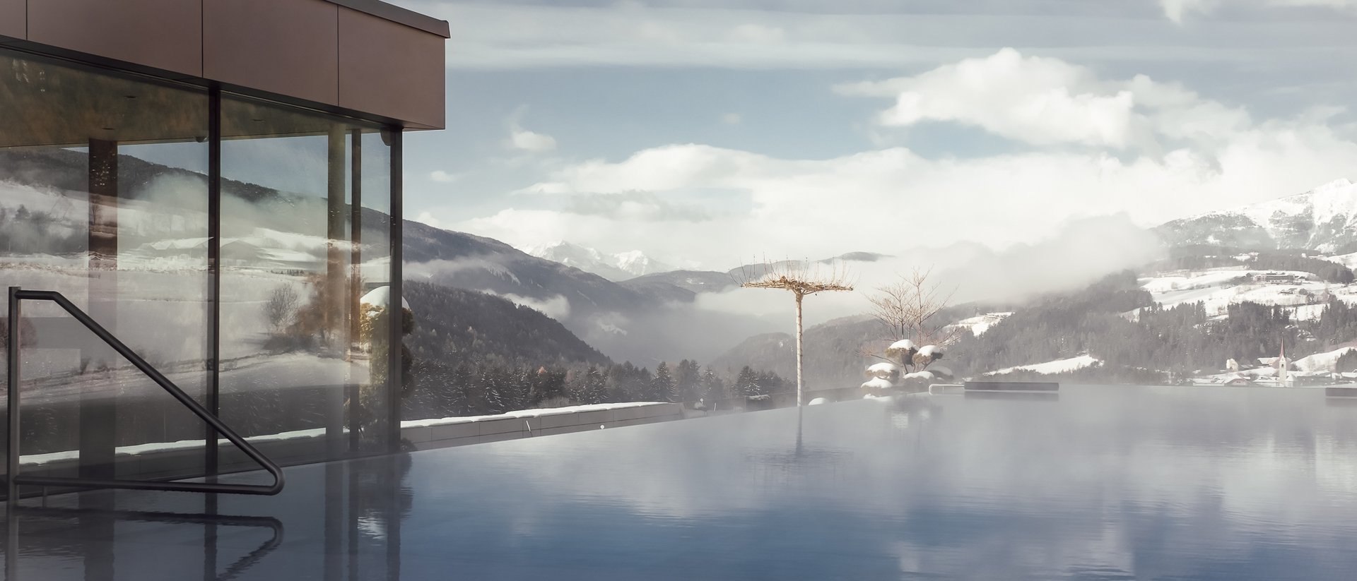 La fonte di ogni luce: il nostro hotel a Falzes Piscina esterna fumante con vista sulle montagne e edificio moderno in vetro