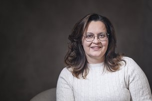 Portrait of a smiling woman wearing glasses and white sweater against a dark background