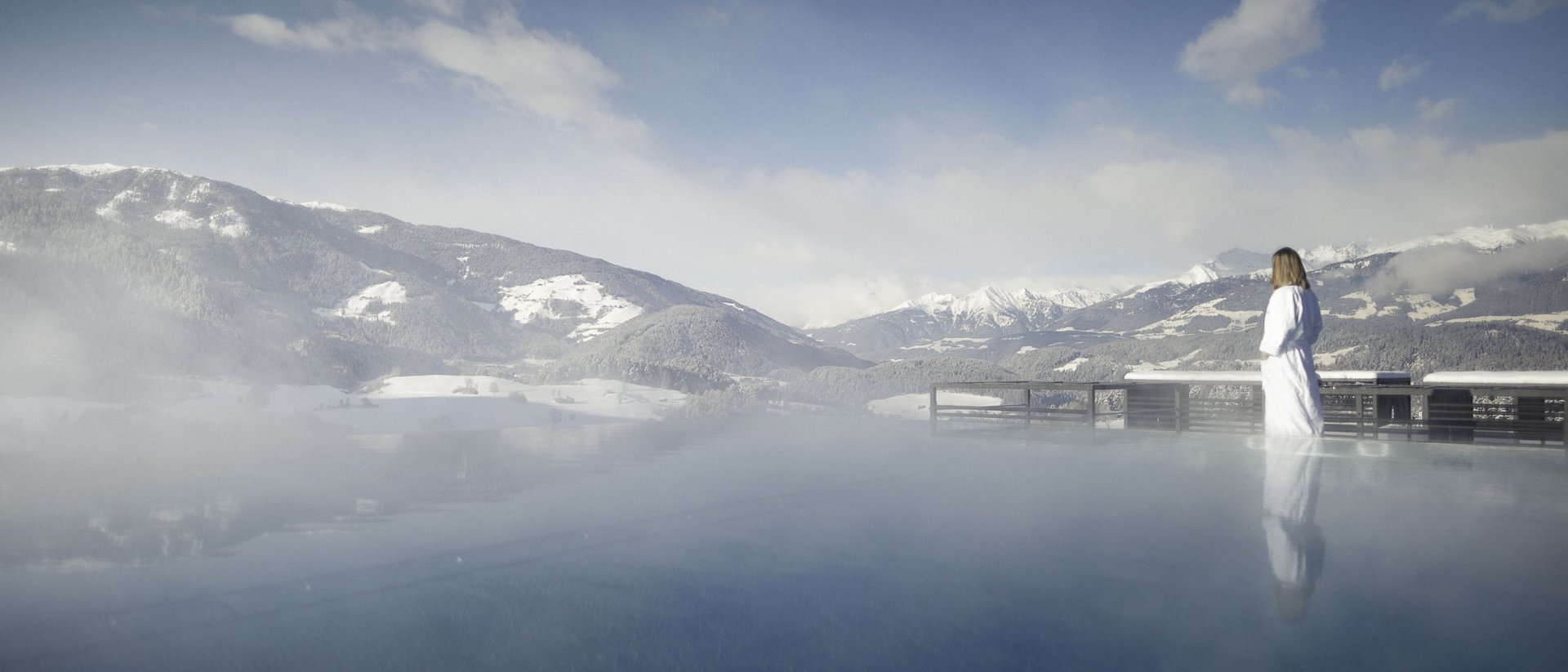 Your source of enrichment: our hotel at Mt Plan de Corones Person in bathrobe standing by steaming pool with mountain view in winter