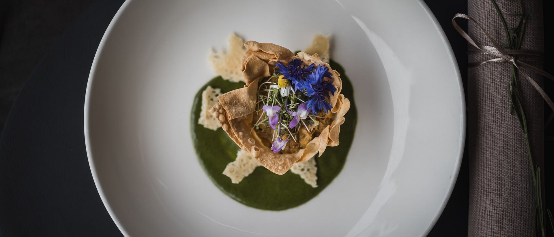 Fein angerichtetes Gericht mit essbaren Blumen und grünem Püree auf weißem Teller