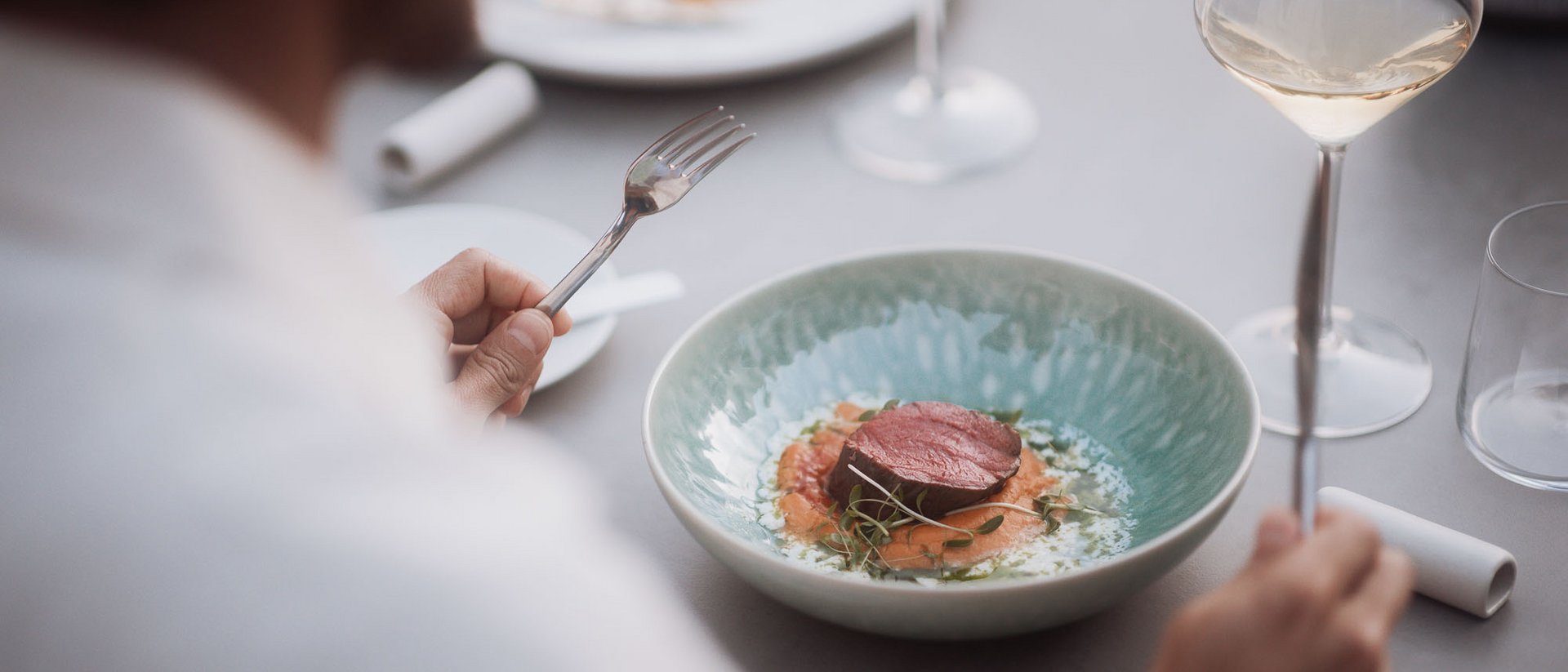 Person isst ein Stück Fleisch auf Gemüse mit Wein im Restaurant