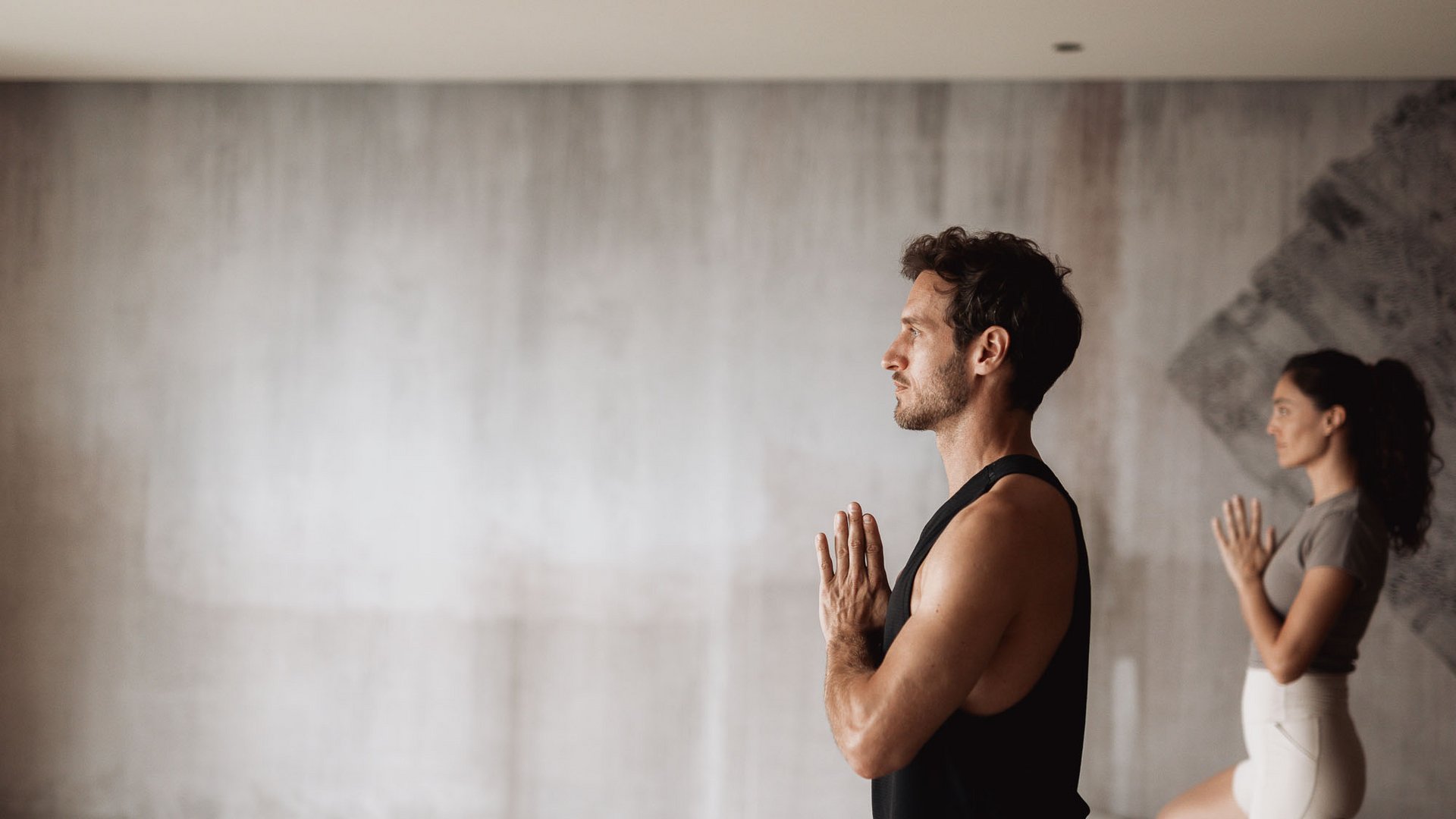 Mann und Frau üben Yoga mit Namaste-Geste und Baum-Pose im Raum