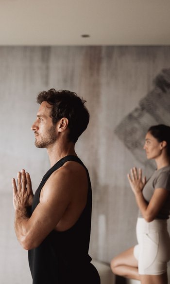 Die Heimat des Strahlens: Ihr Wellnesshotel in Südtirol Mann und Frau üben Yoga mit Namaste-Geste und Baum-Pose im Raum
