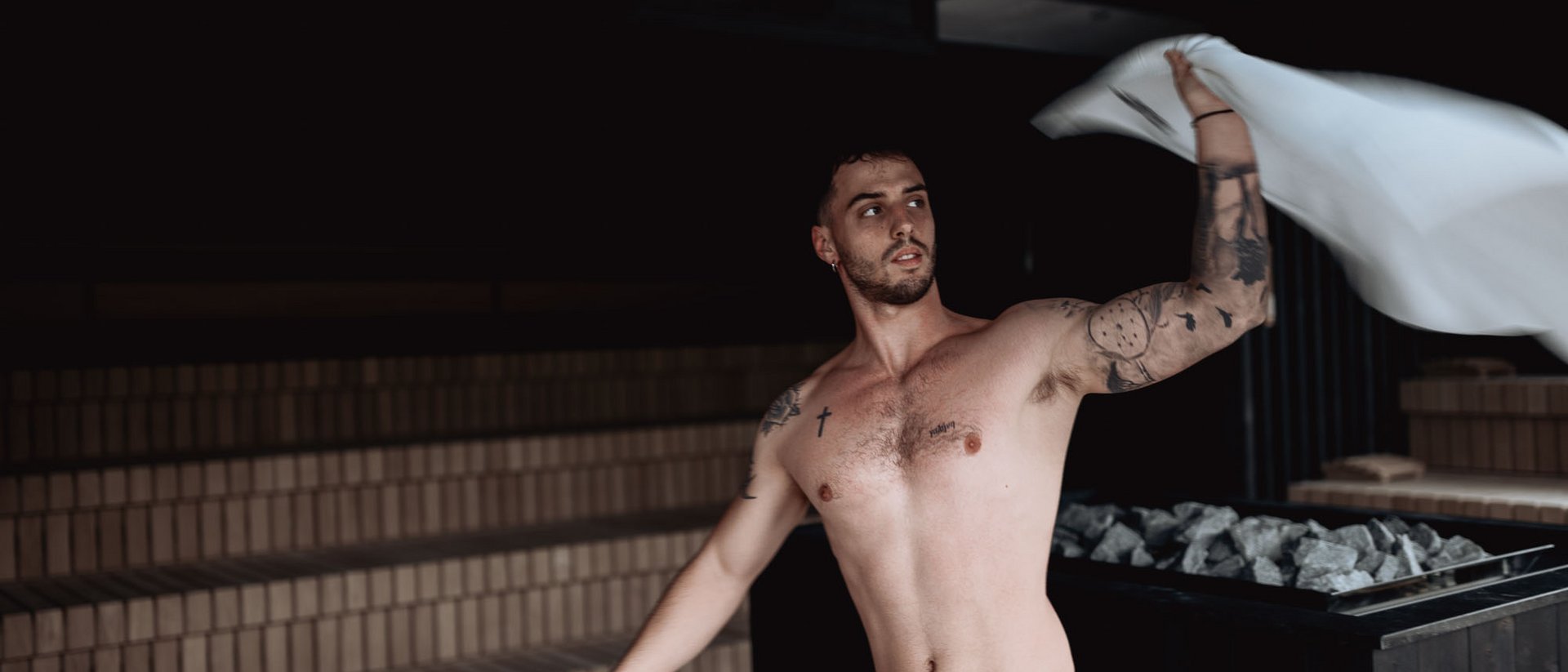 Uomo che agita un asciugamano in sauna con sfondo scuro e fornetto di pietre