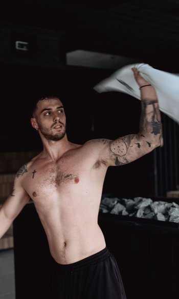 Uomo che agita un asciugamano in sauna con sfondo scuro e fornetto di pietre