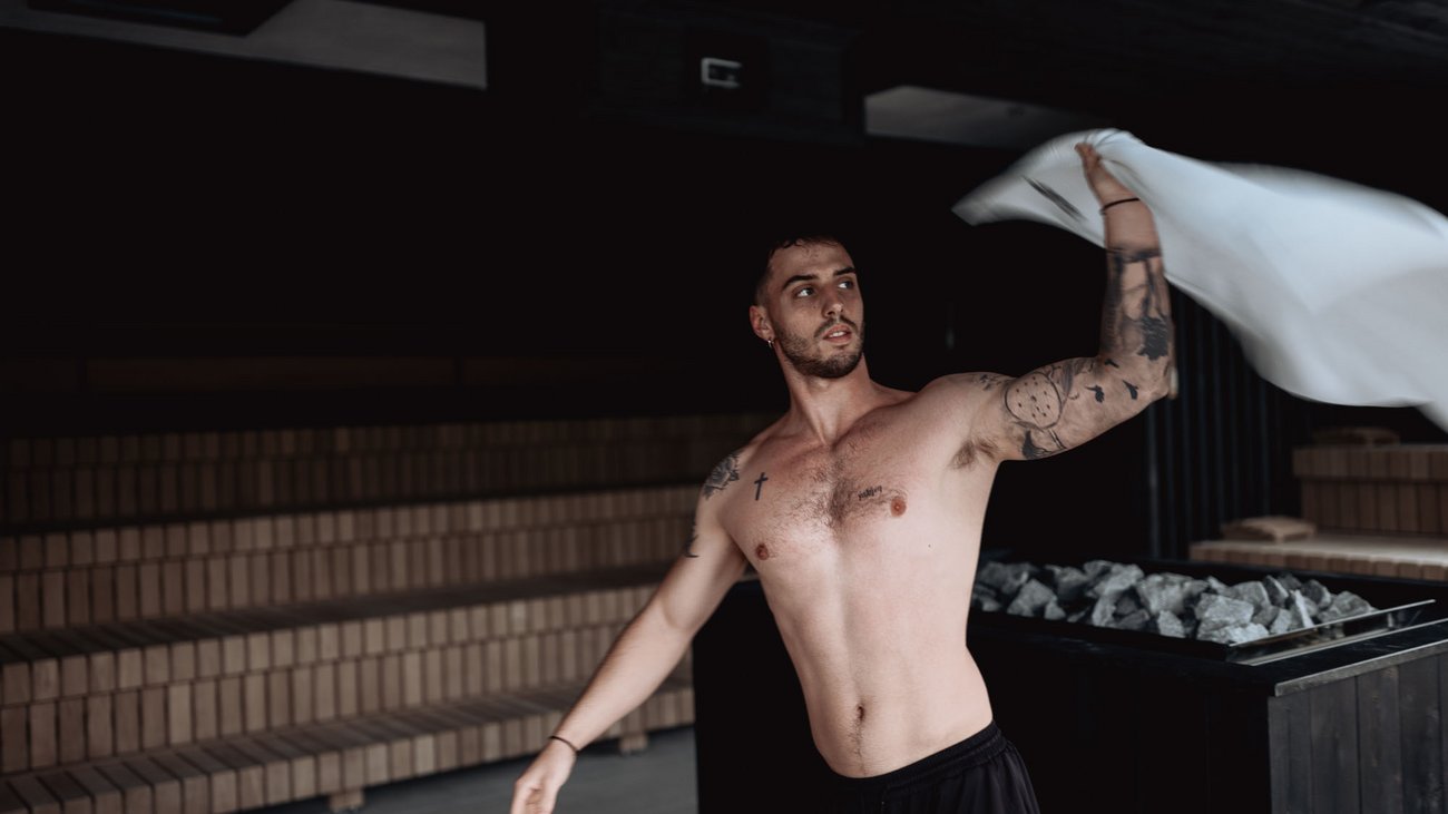 Uomo che agita un asciugamano in sauna con sfondo scuro e fornetto di pietre