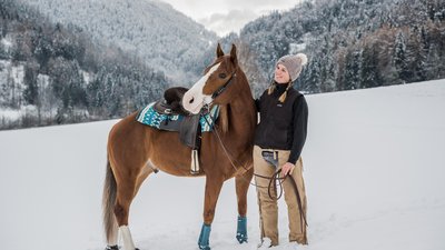 Donna con cavallo nella neve davanti a montagne coperte di alberi