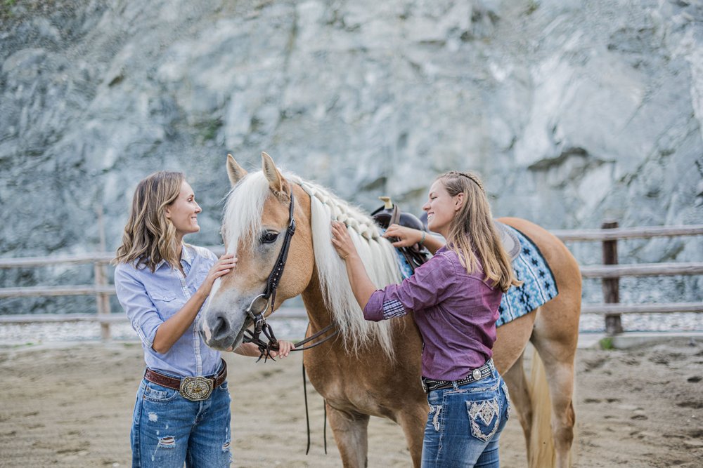 Zwei Frauen beim Streicheln und Pflegen eines hellen Pferdes im Reitstall
