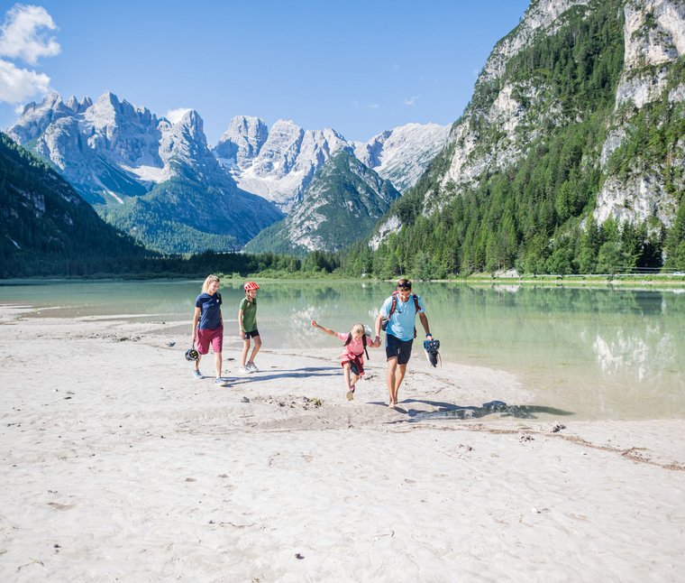 Famiglia cammina a piedi nudi vicino al lago in montagna con cielo soleggiato