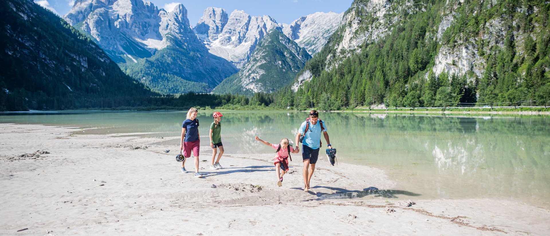 Familie wandert barfuß am See in den Bergen bei sonnigem Wetter