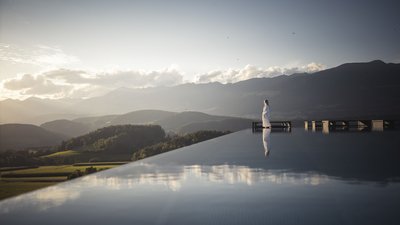 Persona in accappatoio vicino a piscina a sfioro con vista sulle montagne al tramonto