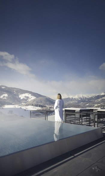 Donna in accappatoio vicino alla piscina sul tetto con vista sulle montagne innevate
