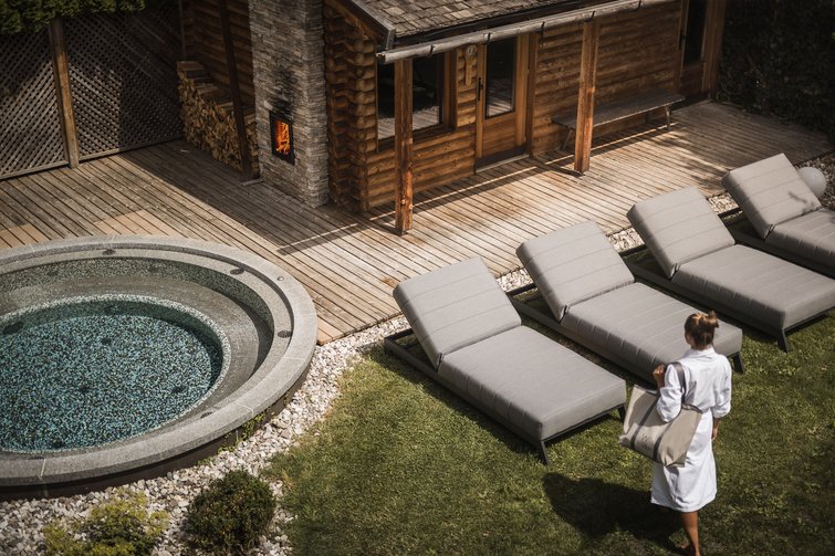 Frau in Bademantel neben Spa-Pool und Liegen vor Holzhütte