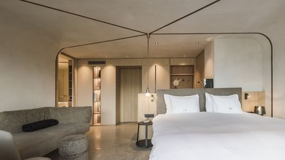 Camera d'hotel moderna con letto matrimoniale e area salotto in colori neutri