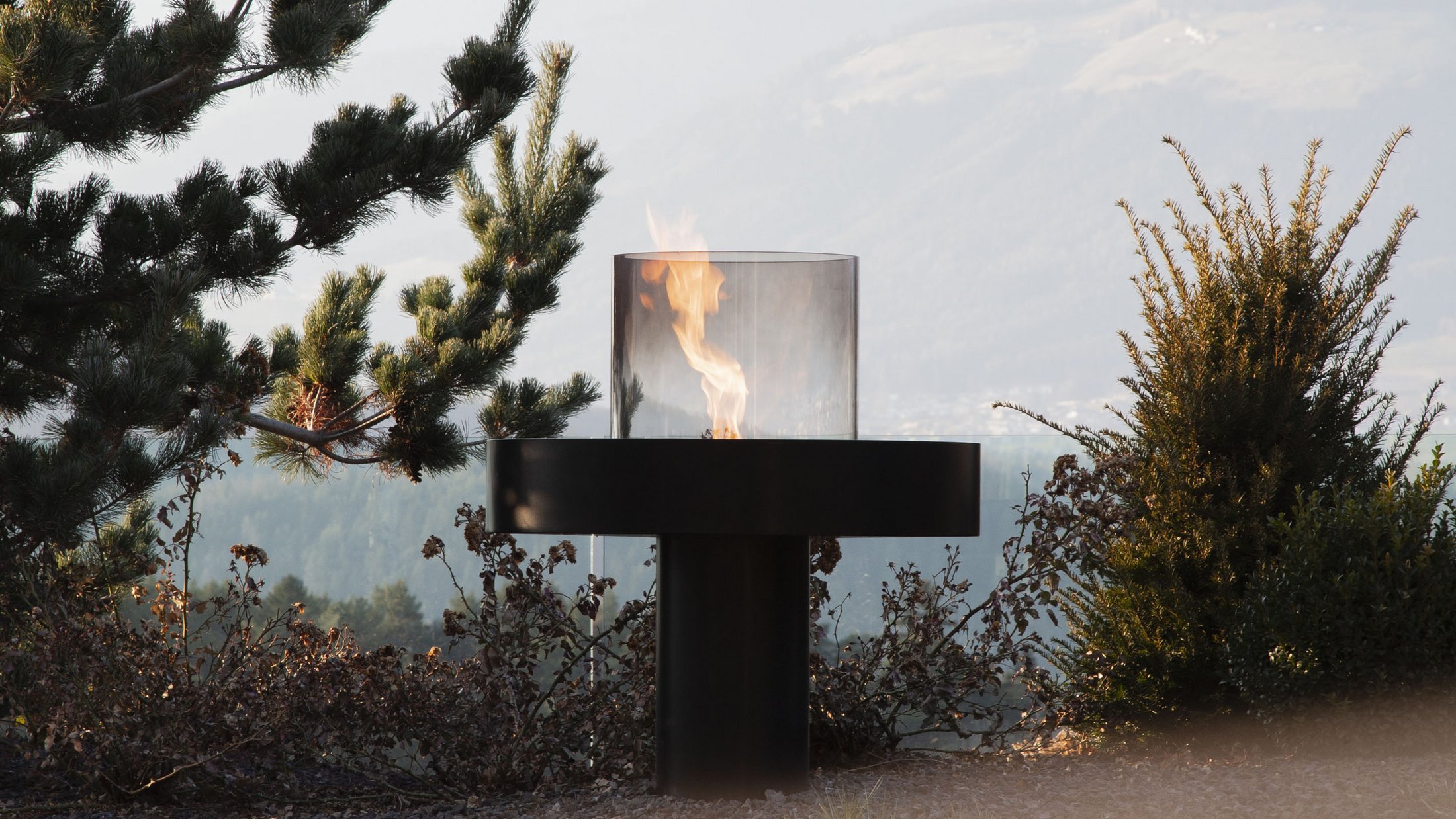 Modern fire pit with flame in garden with mountain view