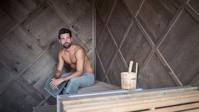 Uomo seduto con asciugamano in una sauna di legno moderna