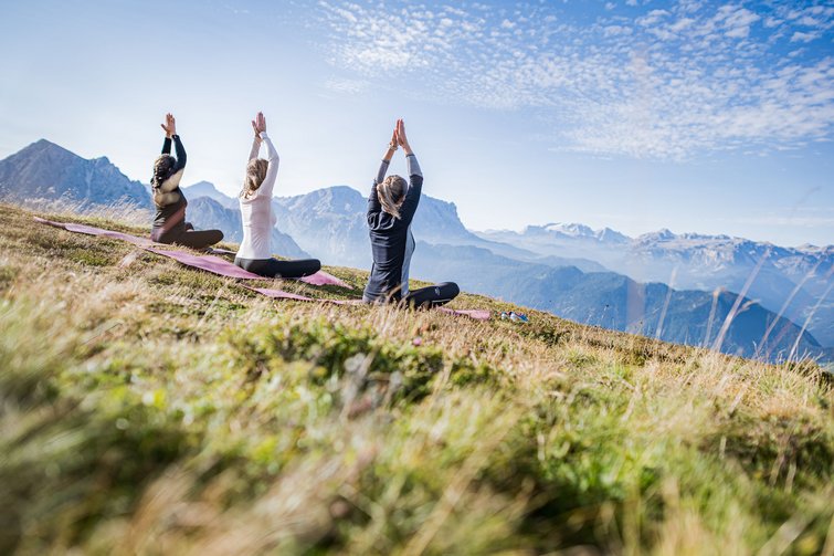 Tre donne fanno yoga su un prato con vista sulle montagne