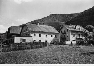 Black and white photo of farmhouses with forested mountains in background