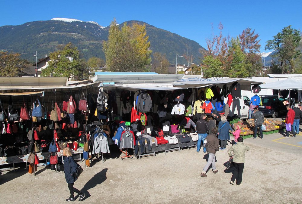 Marktstände mit Kleidung und Taschen vor Bergkulisse an einem sonnigen Tag
