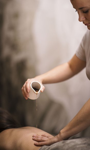 Donna versa olio da massaggio sulla schiena di una persona sdraiata