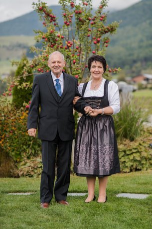 Elderly couple in traditional clothes standing in front of apple tree in countryside