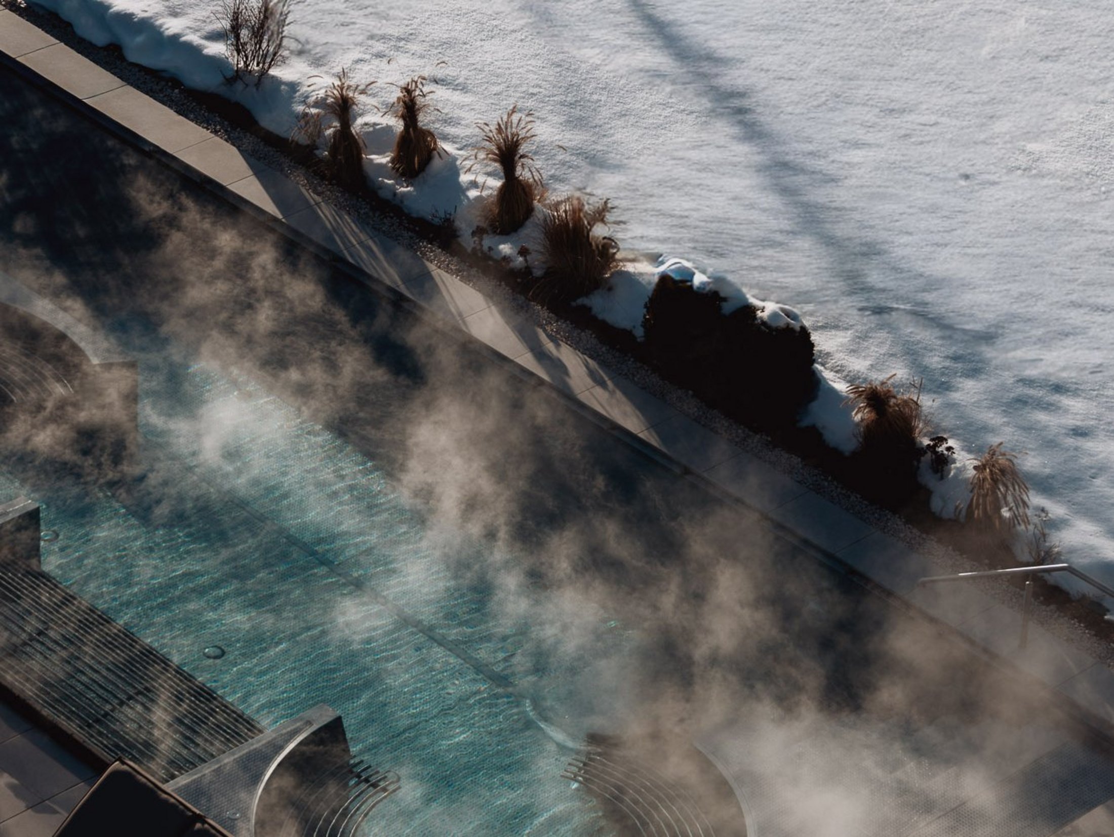 The multi-faceted Sonnenspa at our spa hotel in South Tyrol Steaming outdoor pool beside snow-covered garden in winter