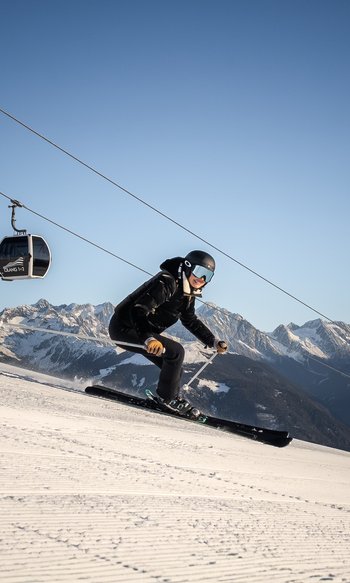 I vostri hotel in Alto Adige: qui dove tutto è possibile Sciatore scende una pista con funivia e montagne innevate sullo sfondo